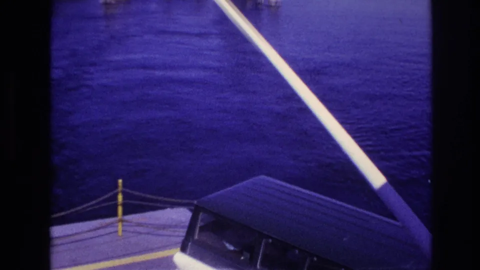 1967 Ottawa-area home-movie frame showing the boat bow, windshield, white rail, open water, and a low distant shoreline.