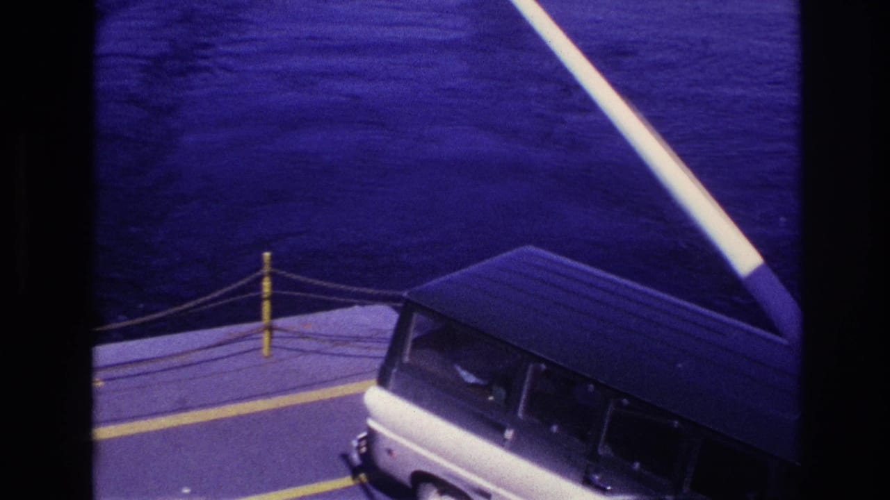 1967 Ottawa-area home-movie frame showing a white van on a ferry deck with yellow markings, rope barriers, and water beyond.
