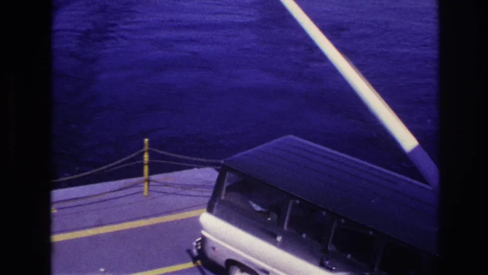 1967 Ottawa-area home-movie frame showing a white van on a ferry deck with yellow markings, rope barriers, and water beyond.