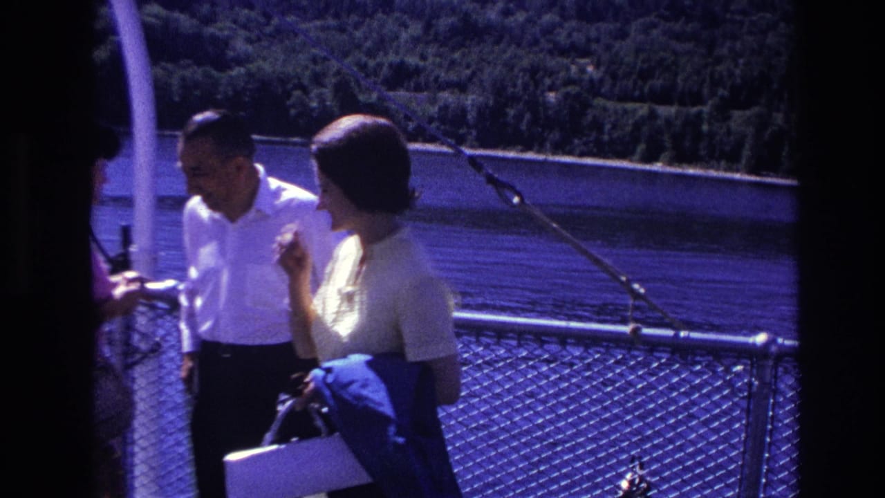 In Ottawa, Canada, in 1967, a man in a white shirt and a woman in a light dress stand near a boat railing by calm water.