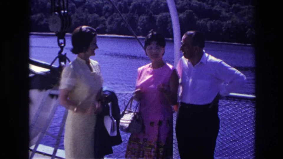 1967 Ottawa home-movie frame showing two women and a man conversing on a boat deck near calm water.
