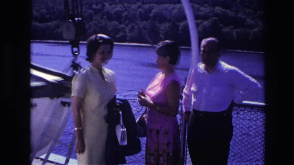 Two women in light summer dresses and a man in a white shirt stand on a boat deck in Ottawa archival footage.