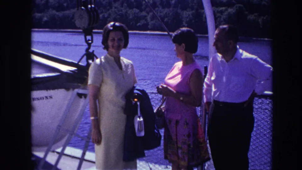 Archival 8mm frame from Ottawa showing three adults on deck, framed by railing, rigging, and blue water.