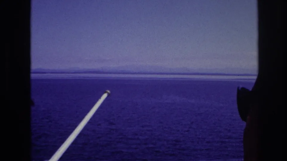 1967 8mm view of water and distant shore through a window frame, with a partial silhouetted person visible along the right edge.