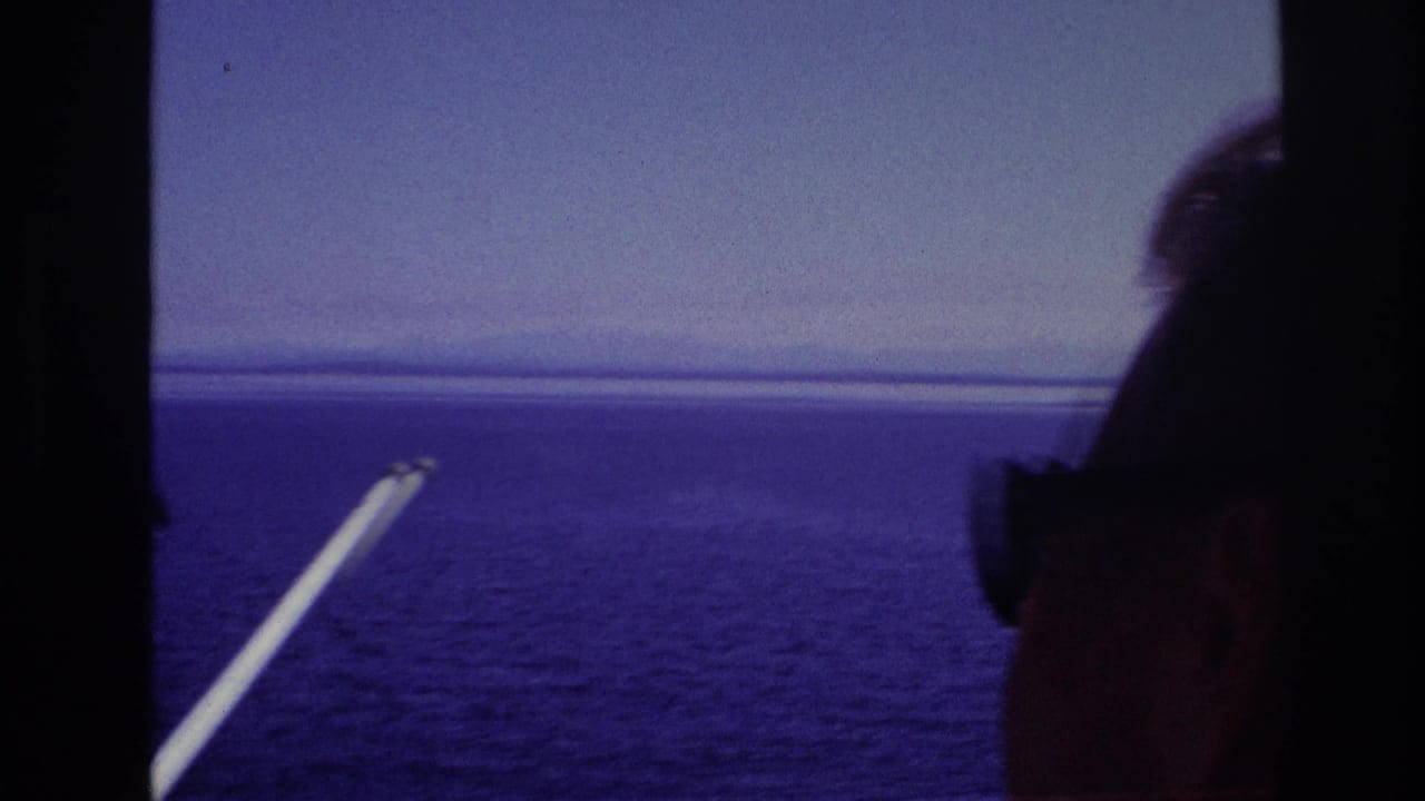 1967 home-movie frame showing passengers in silhouette looking over open water from a moving boat, with a white pole at left.