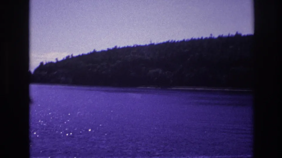 Ottawa-area 8mm frame from 1967 showing purple-tinted water and a wooded shoreline beyond dark window or gate edges.