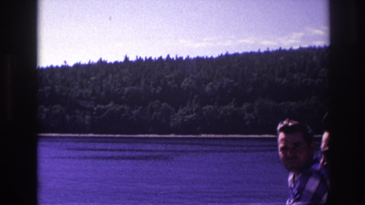 1967 Ottawa home-movie frame showing a man on a boat with a lake and tree-covered hillside in the background.