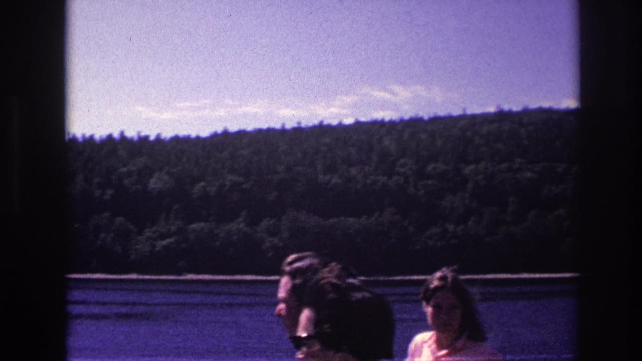1967 Ottawa frame with several boat passengers partly visible against a lake, forested hillside, and bright sky.