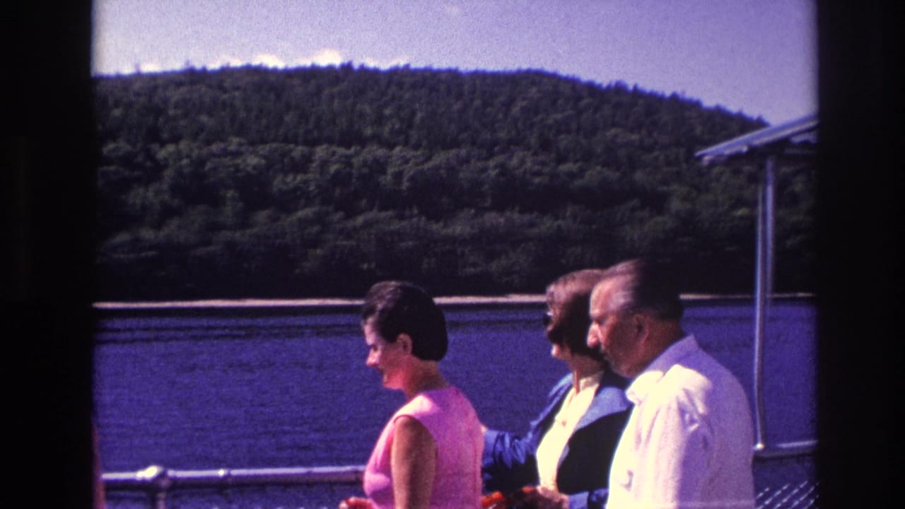 Adults standing on a boat deck beside a river and forested hillside.