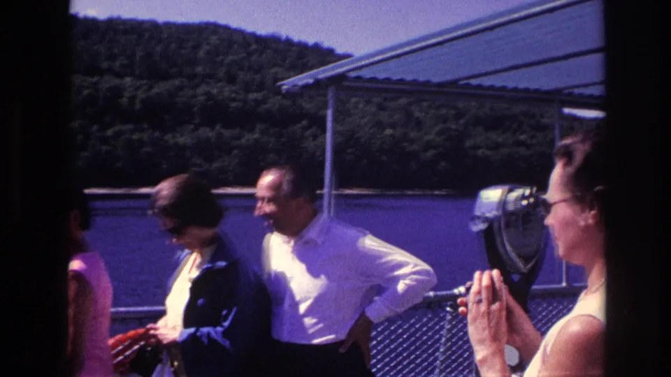 1967 Ottawa frame with adults on a boat deck, a mounted viewer or deck fixture, railing, river, and forested hillside visible.