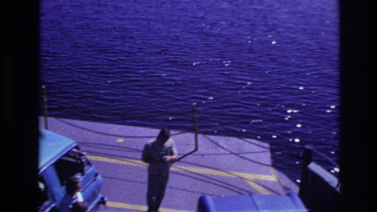 1967 Ottawa ferry scene with a man holding a bag beside the partial roof of a blue car and sunlit water in the background.