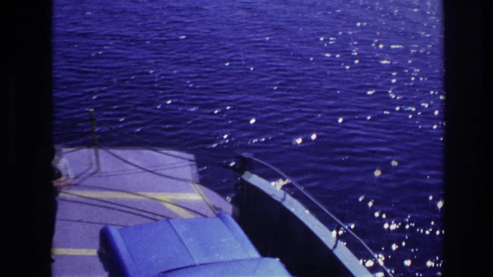 1967 Ottawa home-movie frame showing rippling water, ferry deck markings, railing, and part of a blue car during the crossing.