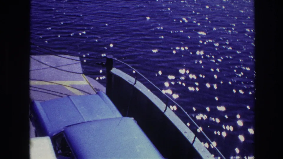 1967 Ottawa ferry frame with the blue car roof in the foreground, railings to the side, and sparkling water beyond.