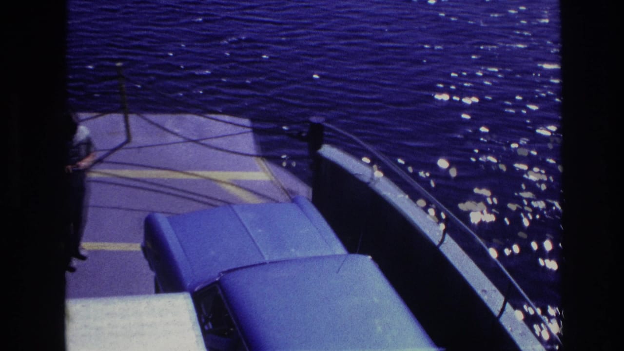 1967 Ottawa home-movie frame showing a blue van on a ferry deck near railings, with dark water and sunlight beyond.