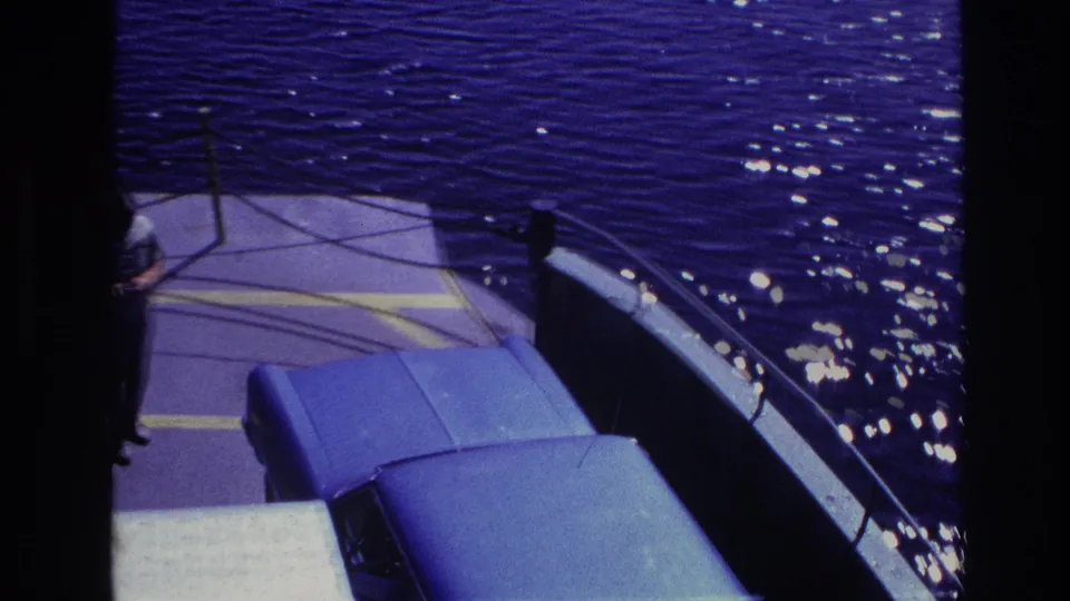 1967 Ottawa home-movie frame showing a blue van on a ferry deck near railings, with dark water and sunlight beyond.