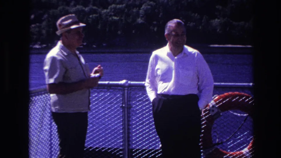 Two men stand in profile and face-forward near a waterfront railing in 1967 Ottawa home-movie footage.