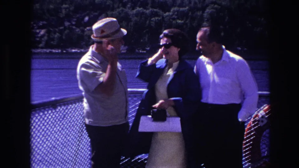 In Ottawa 1967 home-movie footage, three adults stand near a chain-link railing on a boat deck with water and trees behind them.
