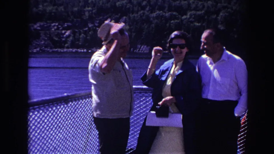 A man adjusts or lifts his hat as the woman laughs, capturing a candid 1967 Ottawa boat-deck moment by the water.