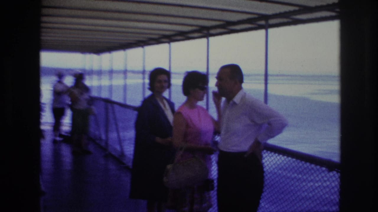 Three adults stand on a covered boat deck beside windows overlooking water.
