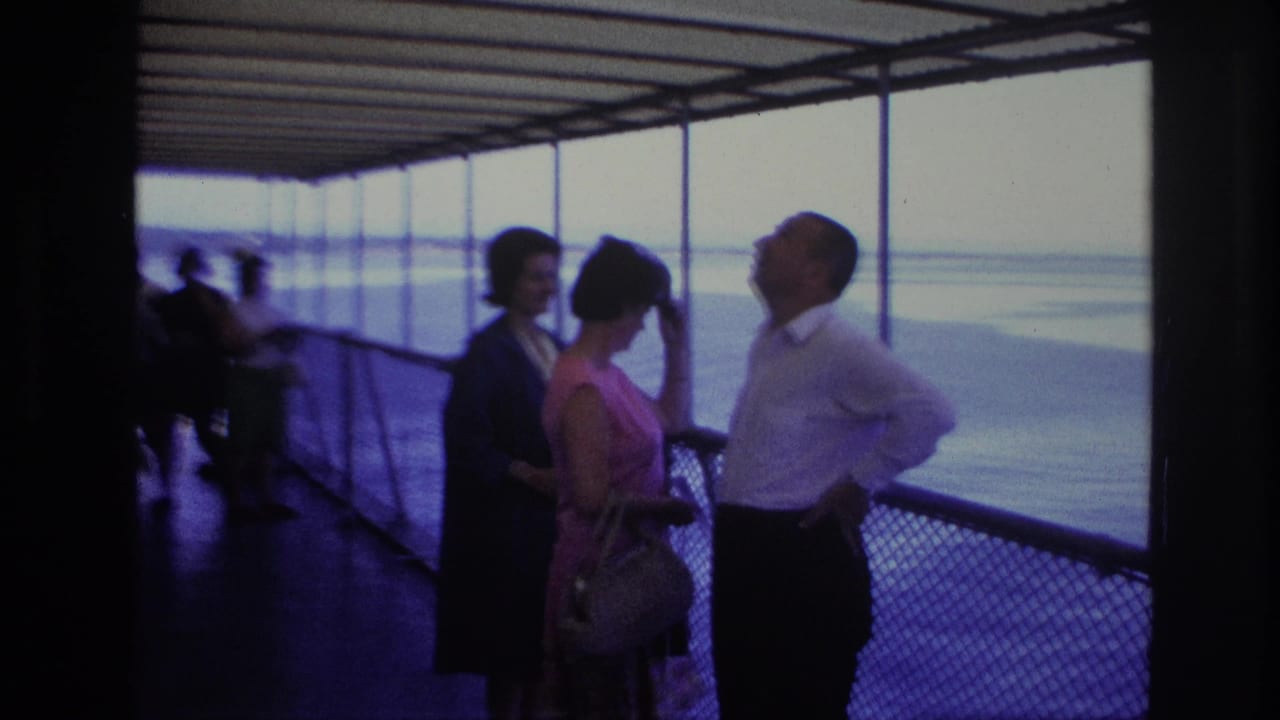 On a 1967 Ottawa boat ride, a man in a white shirt gestures as two women stand near the railing and look toward him and the water.