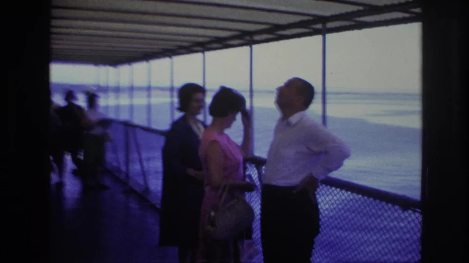 On a 1967 Ottawa boat ride, a man in a white shirt gestures as two women stand near the railing and look toward him and the water.