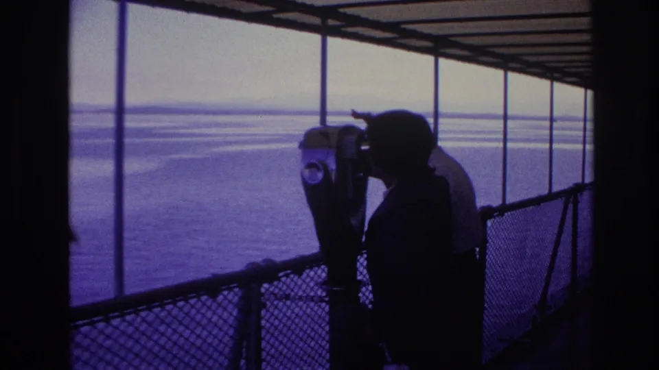 1967 Ottawa home-movie still showing a silhouetted tourist at a coin-operated viewer on a covered waterfront observation deck.