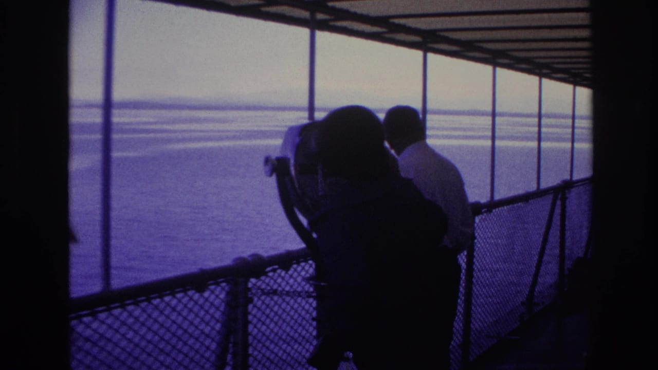 1967 Ottawa home-movie frame showing silhouetted visitors beside a fixed binocular viewer on a covered waterfront pier.