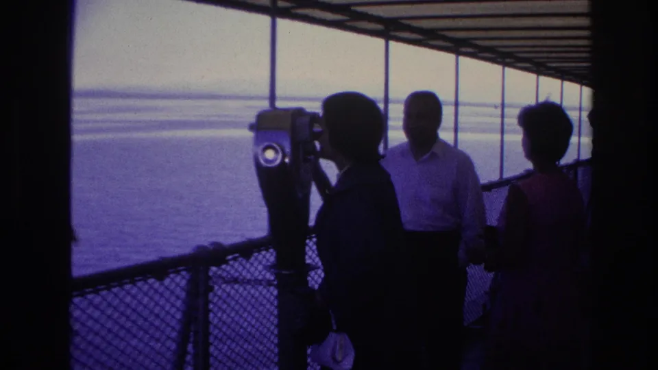1967 Ottawa home-movie frame showing adults in silhouette near a tower viewer on a covered boat deck facing bright water.