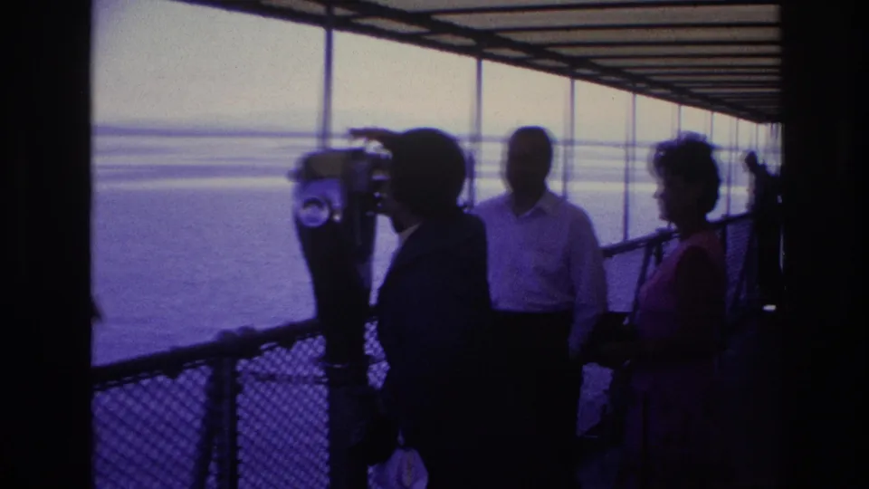 1967 Ottawa footage frame with a woman at a coin-operated viewer, two adults nearby, and open water beyond the deck railing.