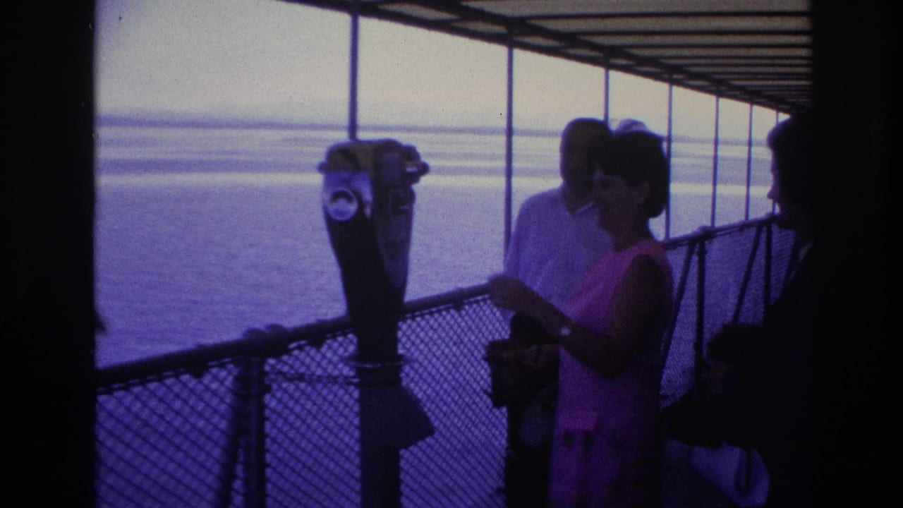 1967 Ottawa home-movie frame showing adults on a covered deck as a woman in pink stands near a binocular viewer overlooking water.