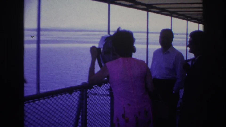 1967 Ottawa home-movie frame of adults on a shaded deck as the woman uses the viewer and others stand near the railing.