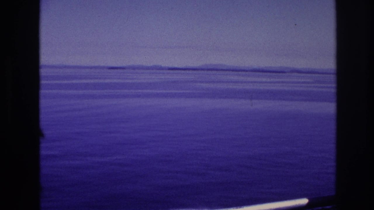1967 home-movie frame showing calm open water, a hazy horizon, and distant land viewed from aboard a vessel.