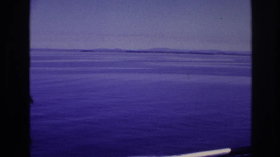 1967 home-movie frame showing calm open water, a hazy horizon, and distant land viewed from aboard a vessel.