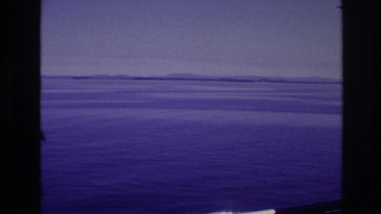 Shipboard 8mm view of calm water and a low distant shoreline under a hazy sky in the supplied 1967 Canada context.