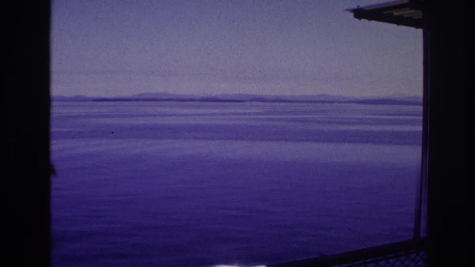 Calm shipboard water view with a hazy horizon and a small section of deck structure entering the frame.