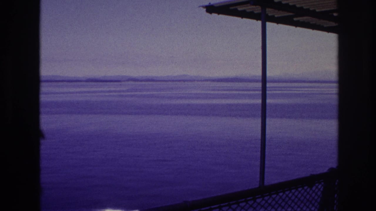 1967 8mm frame from Canada showing open water beyond a covered railing and metal support poles, with no person clearly in view.