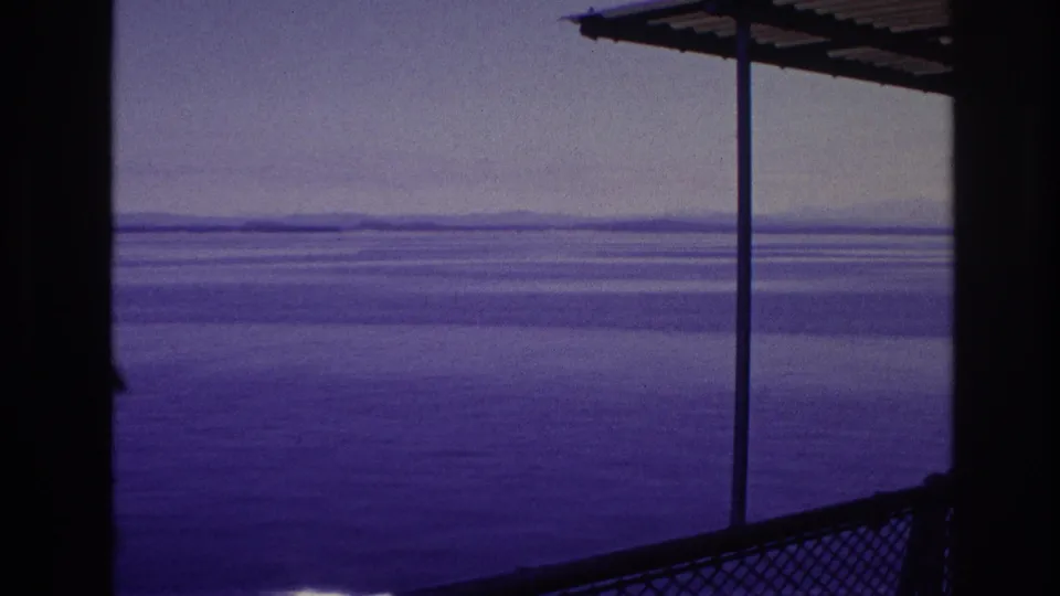 1967 8mm frame from Canada showing open water beyond a covered railing and metal support poles, with no person clearly in view.