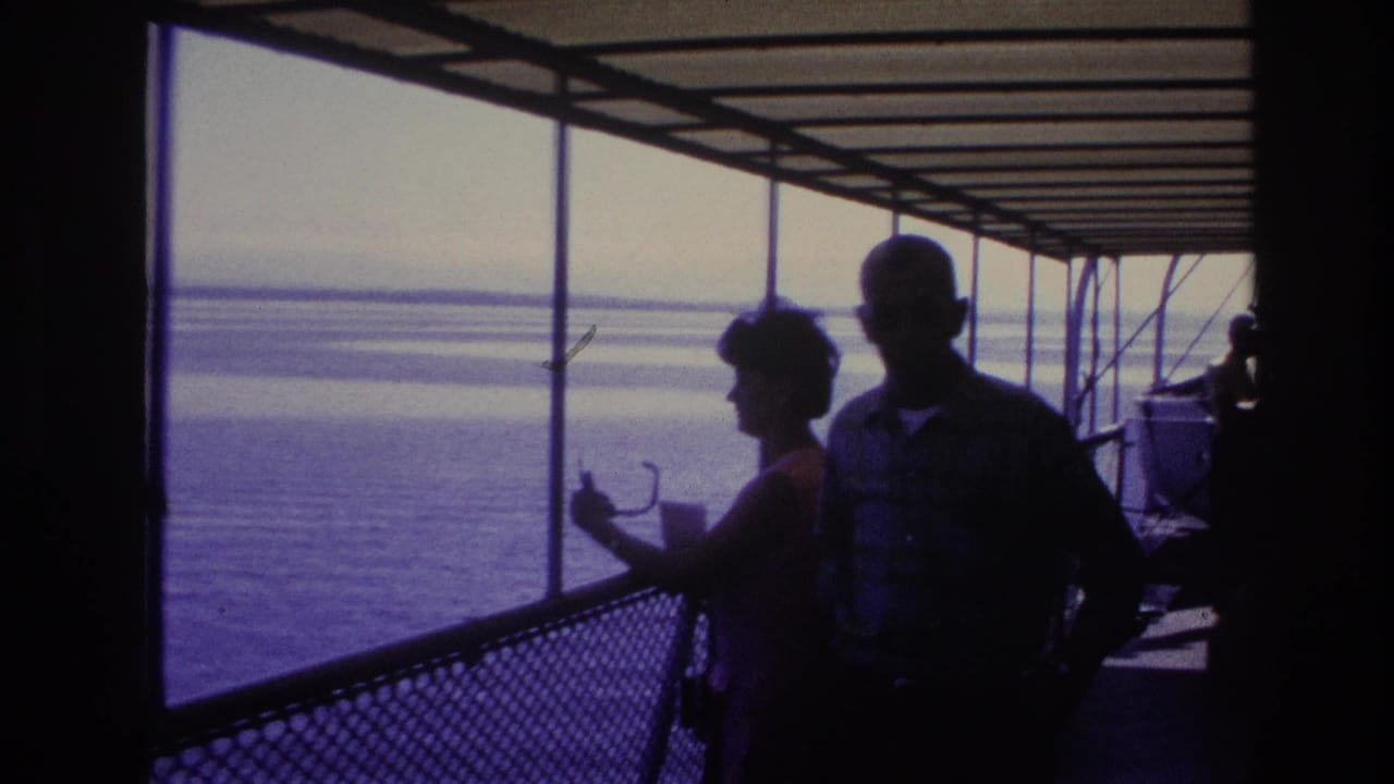 Woman and man stand in silhouette on a covered boat deck beside open water.