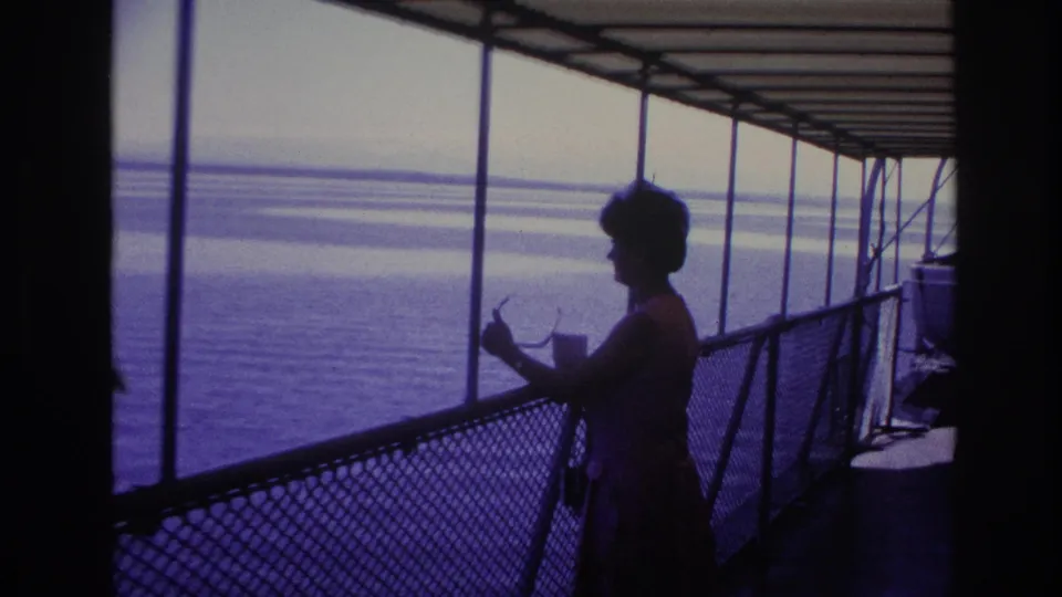 1967 Ottawa home-movie frame showing a silhouetted woman on a covered boat deck with calm water beyond.