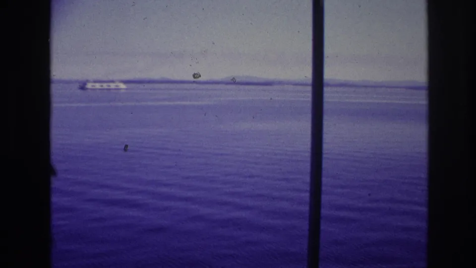 1967 Ottawa, Canada home-movie frame showing purple-tinted water, a distant white passenger ship, and dark window or film-frame bars.