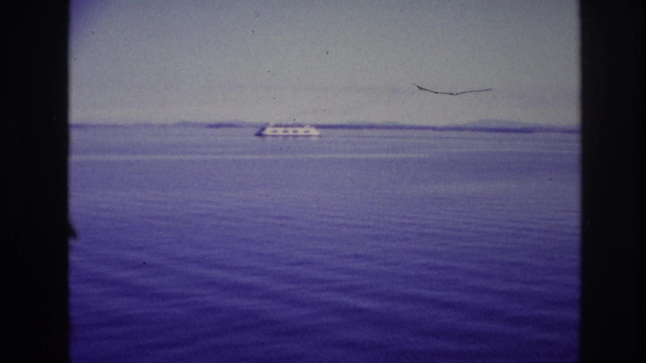 1967 Ottawa, Canada water view with a low white ship near the horizon, purple-blue film color, and dark framing bars in the foreground.