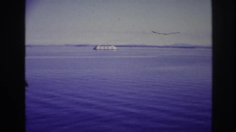 1967 Ottawa, Canada water view with a low white ship near the horizon, purple-blue film color, and dark framing bars in the foreground.