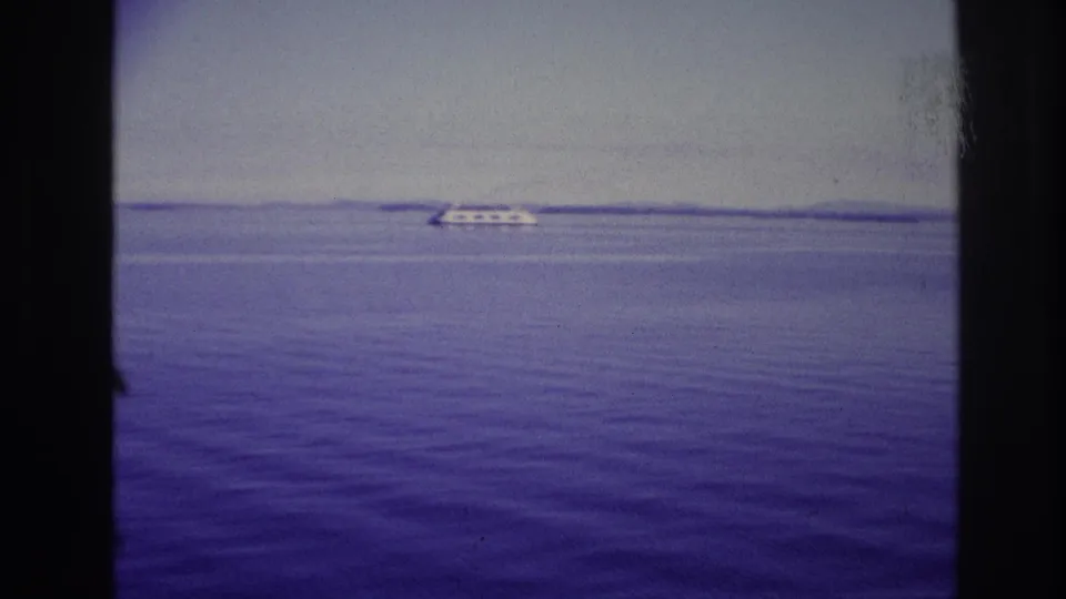 1967 Ottawa, Canada home-movie view of a small white ship against a flat horizon, seen through dark framing with soft 8mm grain.