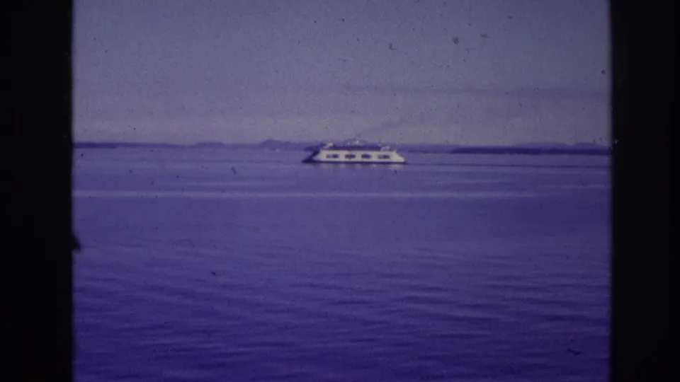 1967 Ottawa-area home-movie frame showing a distant white passenger vessel crossing calm water under a muted sky.