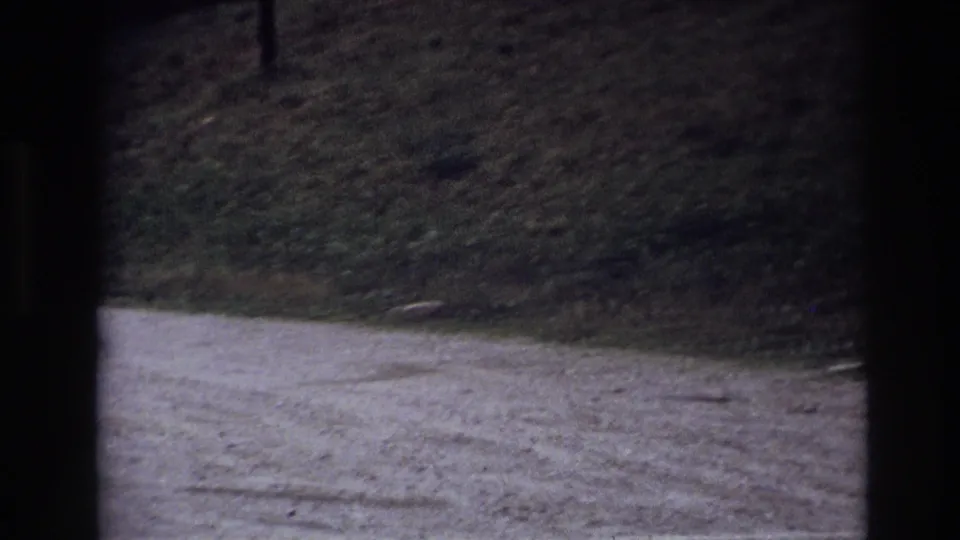 1967 Ottawa home-movie frame showing a gravel path and grassy bank through dark vertical window framing.