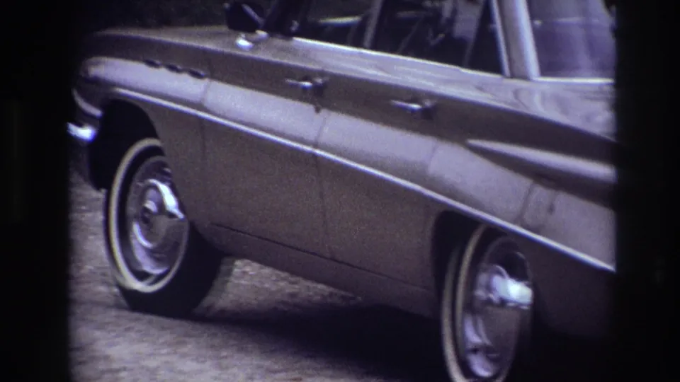 A tan 1960s sedan crosses the 1967 Ottawa frame, with chrome trim and whitewall tires visible through the window.