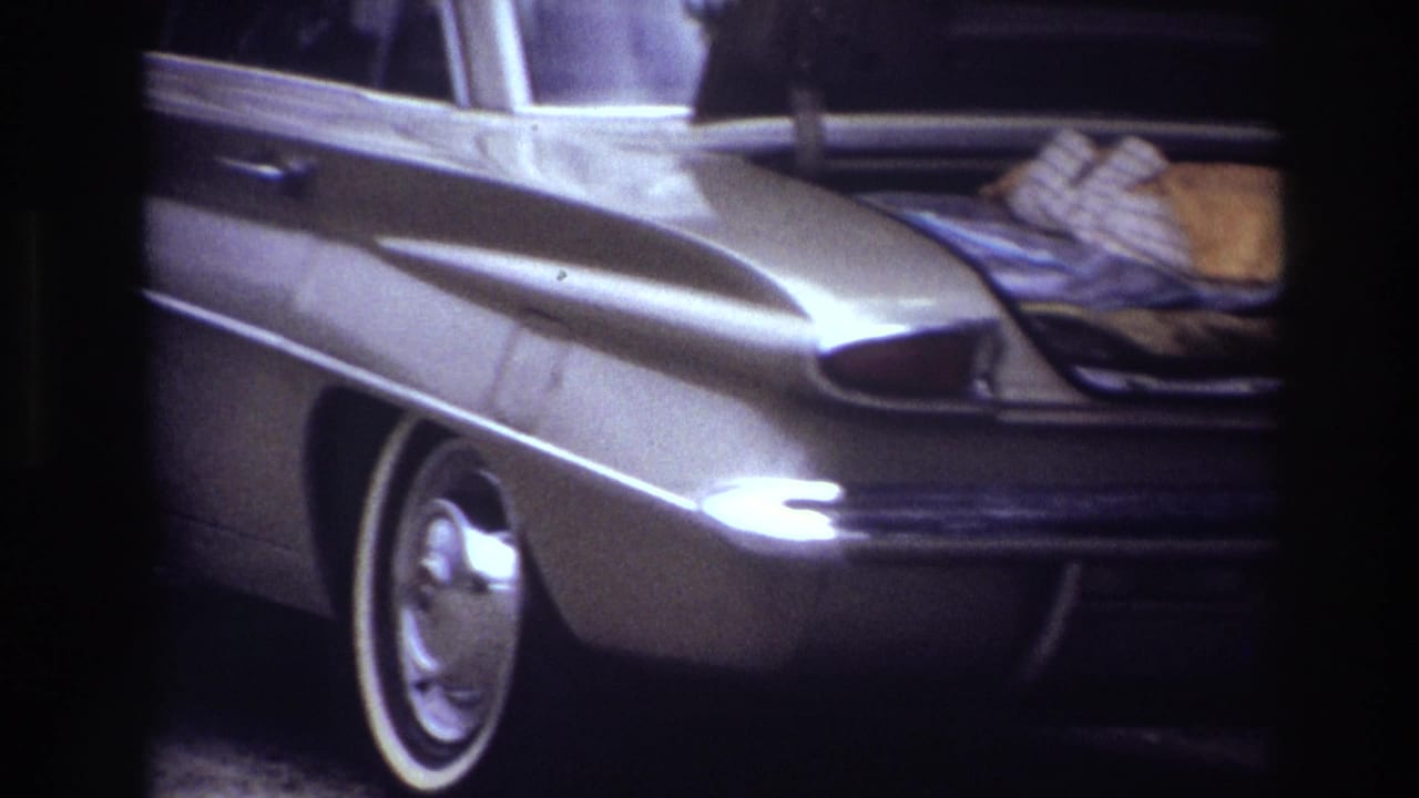 1967 Ottawa home-movie frame showing the side and rear of a classic sedan with an open trunk and packed items inside.