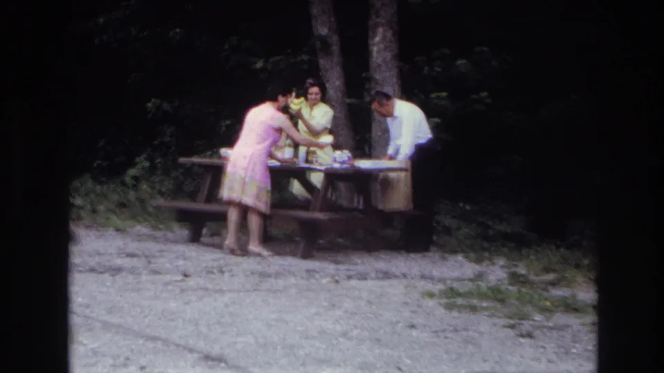 The home-movie frame shows three adults setting out picnic items at a table in a wooded Ottawa setting supported by the clip metadata.