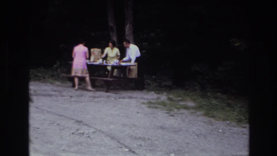 A wider 8mm frame shows the picnic table and three adults from farther back in the supplied 1967 Ottawa home-movie scene.