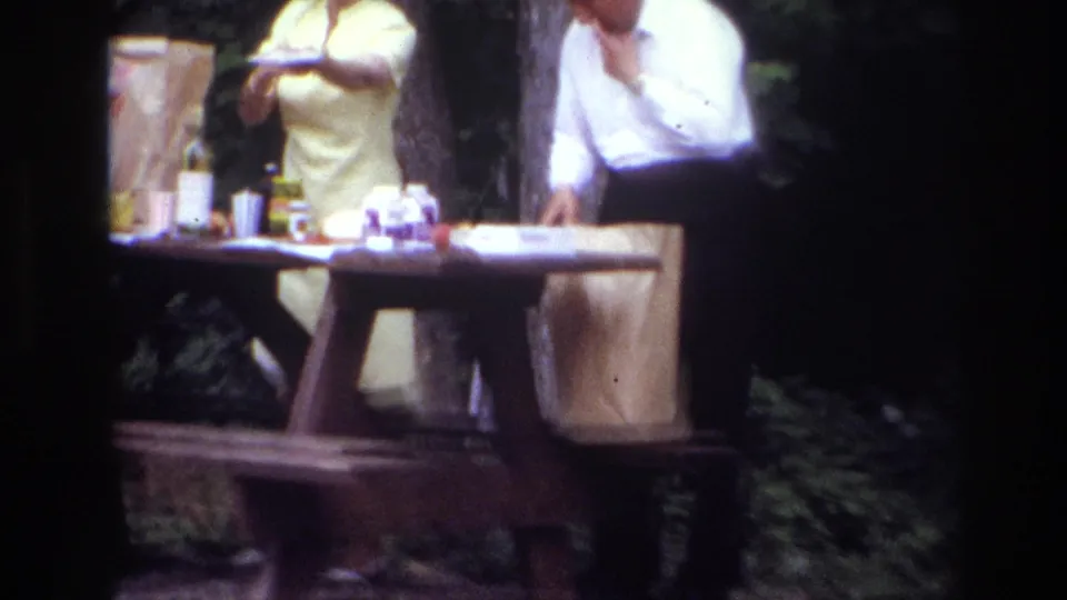 Closer 8mm view of adults preparing a picnic table in an Ottawa park, with bags and small containers visible.